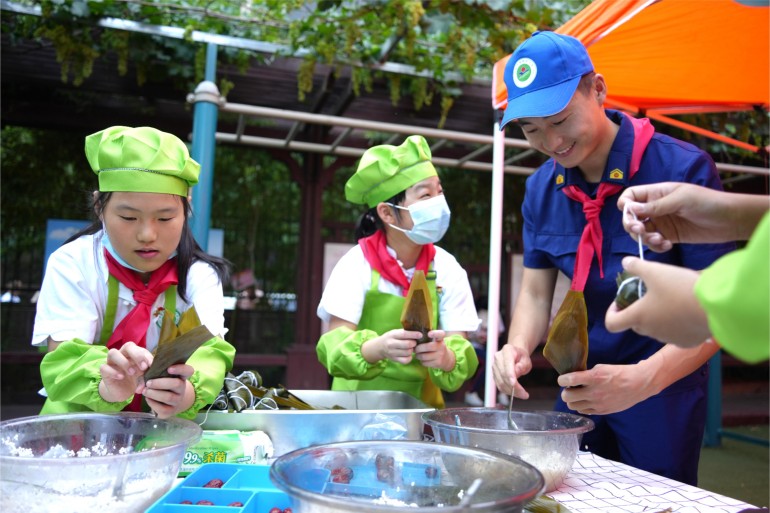 6月21日，濟南館驛街小學舉辦“皂莢樹下話端午”公益愛心主題活動。校內(nèi)幾棵皂莢樹下，市中消防大隊的“藍朋友”們和少先隊員們一起體驗著包粽子的時光。張源源 陳志偉攝