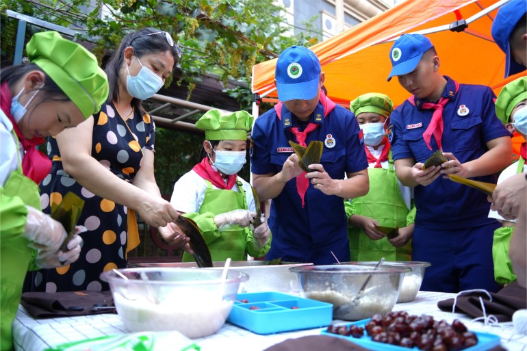 6月21日，濟南館驛街小學(xué)舉辦“皂莢樹下話端午”公益愛心主題活動。校內(nèi)幾棵皂莢樹下，市中消防大隊的“藍朋友”們和少先隊員們一起體驗著包粽子的時光。張源源 陳志偉攝