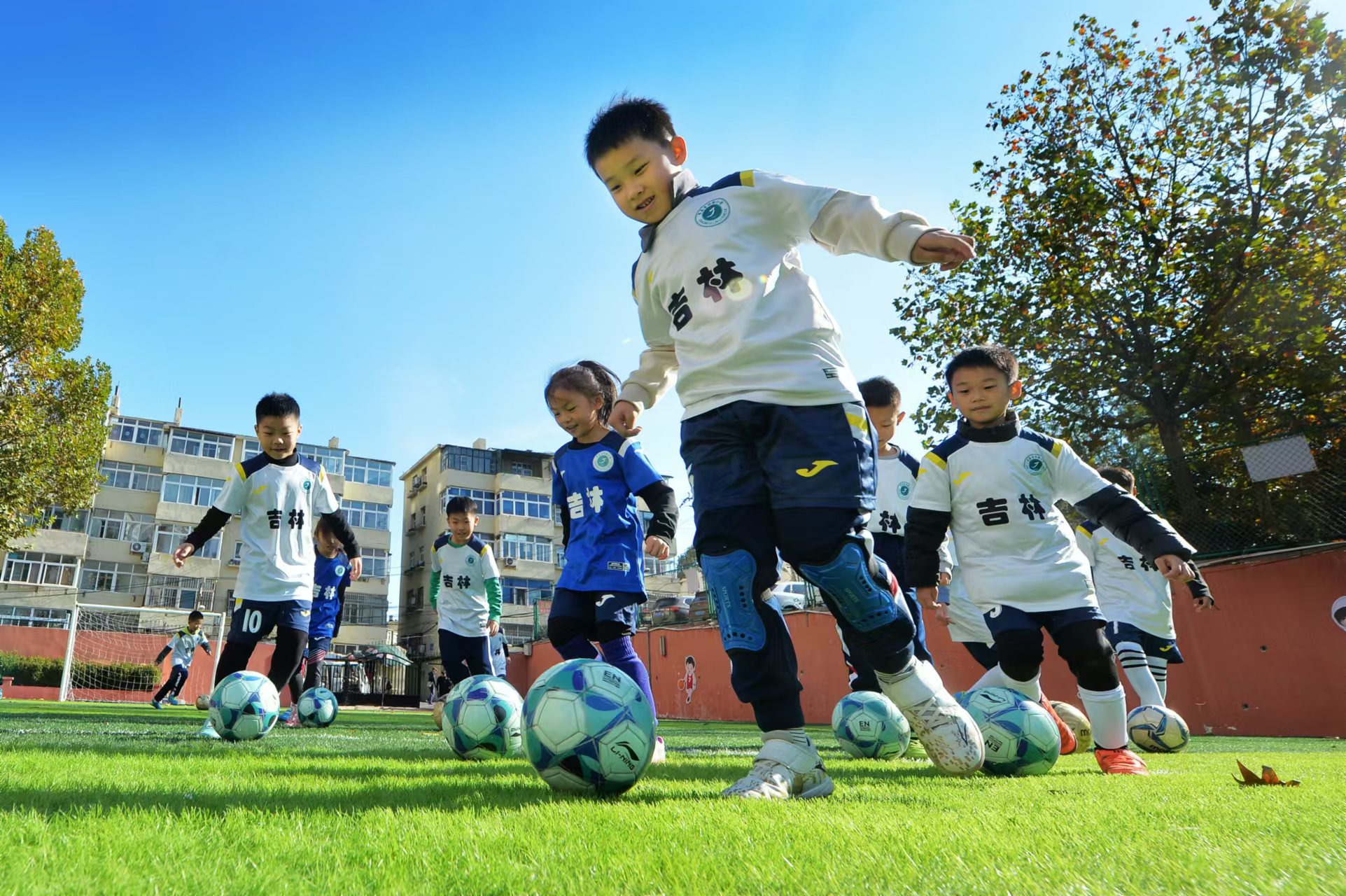 2024年11月18日，在山東青島吉林路小學開展的足球冬訓活動上，孩子們在綠茵場上進行帶球訓練。